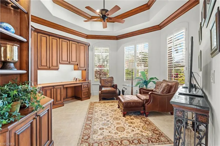 Living area featuring ceiling fan, a tray ceiling, light tile patterned flooring, ornamental molding, and built in desk