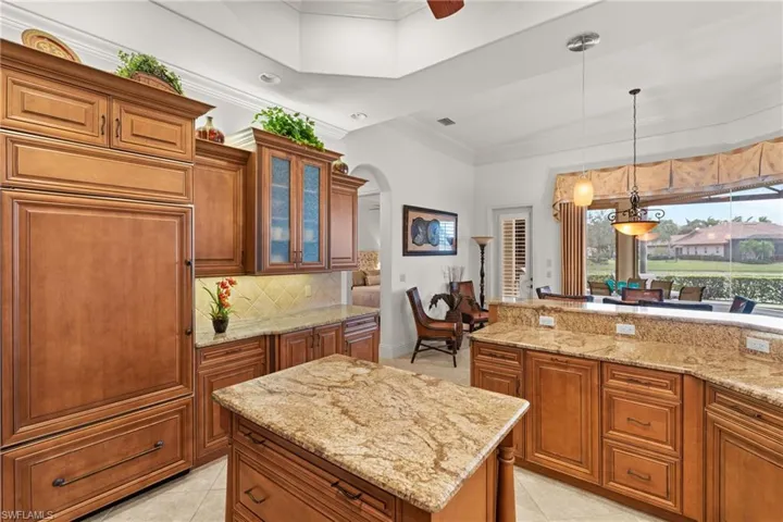 Kitchen with a kitchen island, decorative backsplash, hanging light fixtures, light tile patterned flooring, and light stone counters