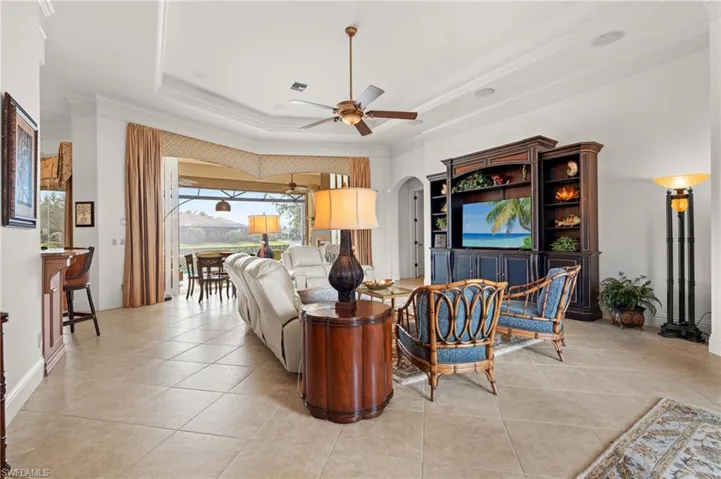 Living room featuring ceiling fan, a raised ceiling, crown molding, and light tile patterned floors