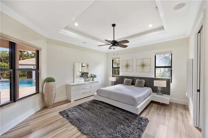 Bedroom with light wood-style floors, a tray ceiling, ornamental molding, multiple windows, and a ceiling fan