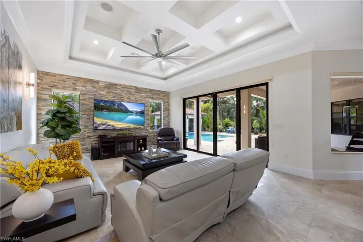 Living room featuring coffered ceiling, ceiling fan, beamed ceiling, an accent wall, and crown molding