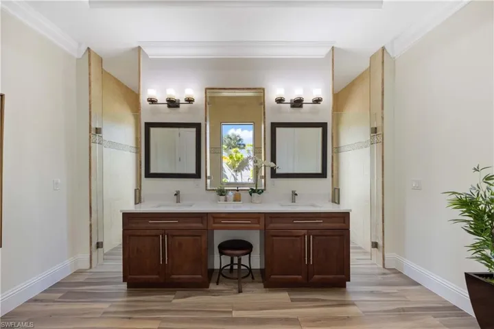Bathroom featuring double vanity, light wood finished floors, a stall shower, and crown molding