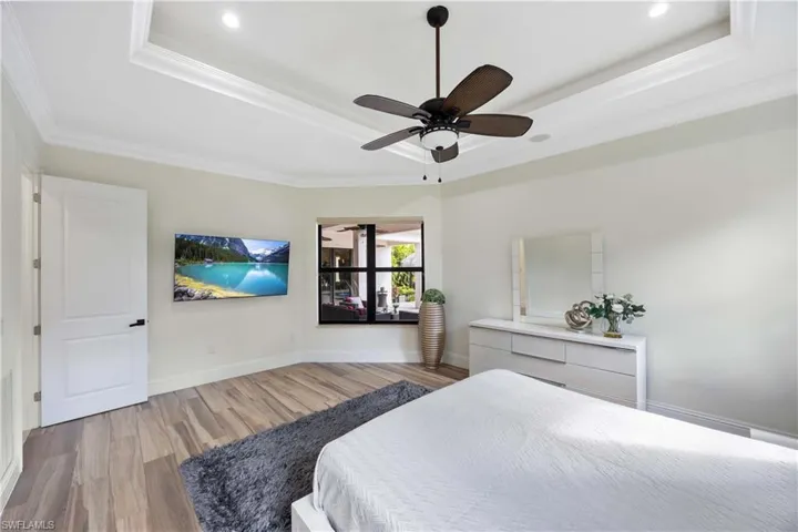 Bedroom with a raised ceiling, wood finished floors, a ceiling fan, and ornamental molding