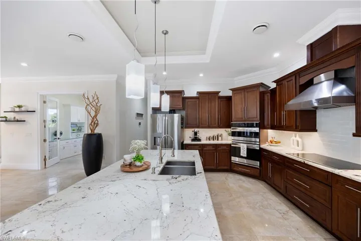 Kitchen featuring decorative light fixtures, wall chimney range hood, backsplash, light stone counters, and appliances with stainless steel finishes