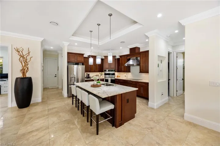 Kitchen featuring a breakfast bar area, a kitchen island with sink, crown molding, pendant lighting, and light stone counters