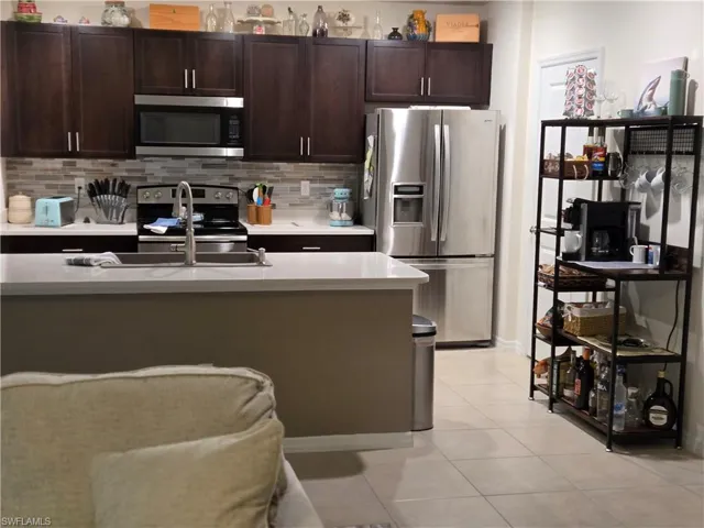 Kitchen featuring appliances with stainless steel finishes, light tile patterned flooring, dark brown cabinets, and tasteful backsplash