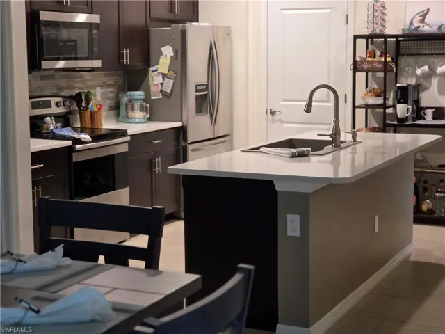Kitchen featuring stainless steel appliances, light countertops, light tile patterned flooring, decorative backsplash, and a kitchen island with sink