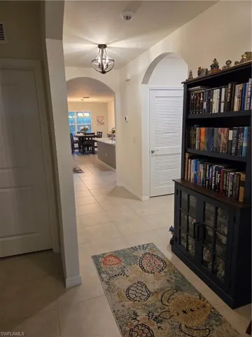Hall featuring arched walkways, a chandelier, and light tile patterned floors