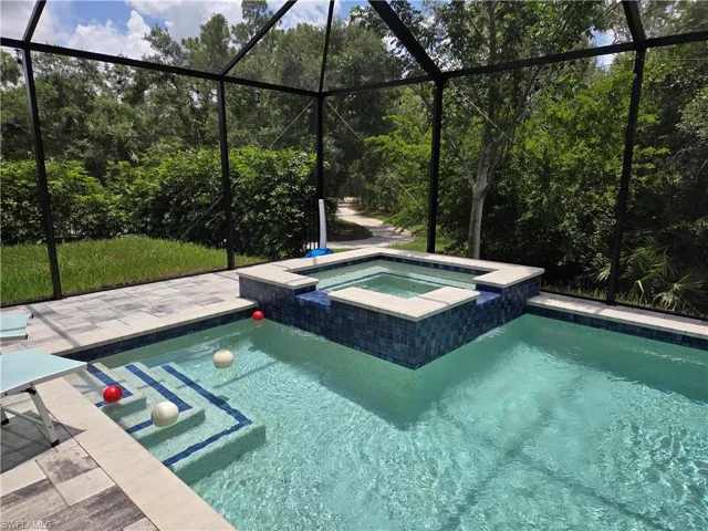View of swimming pool featuring glass enclosure and a pool with connected hot tub