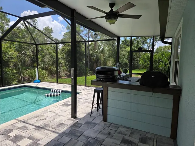 Outdoor pool featuring a patio, grilling area, glass enclosure, and ceiling fan