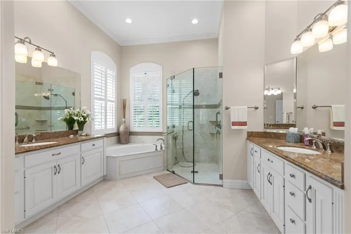 Bathroom with crown molding, light tile patterned floors, a bath, two vanities, and a shower stall
