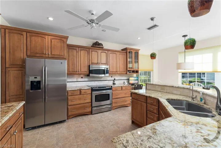 Kitchen with glass insert cabinets, stainless steel appliances, brown cabinetry, decorative light fixtures, and backsplash
