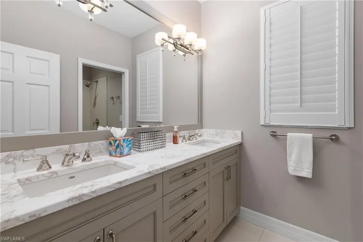 Full bathroom with double vanity, light tile patterned floors, a shower, and a chandelier
