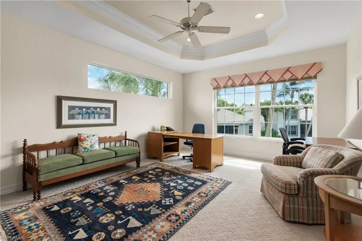 Office space with a raised ceiling, plenty of natural light, carpet flooring, and crown molding