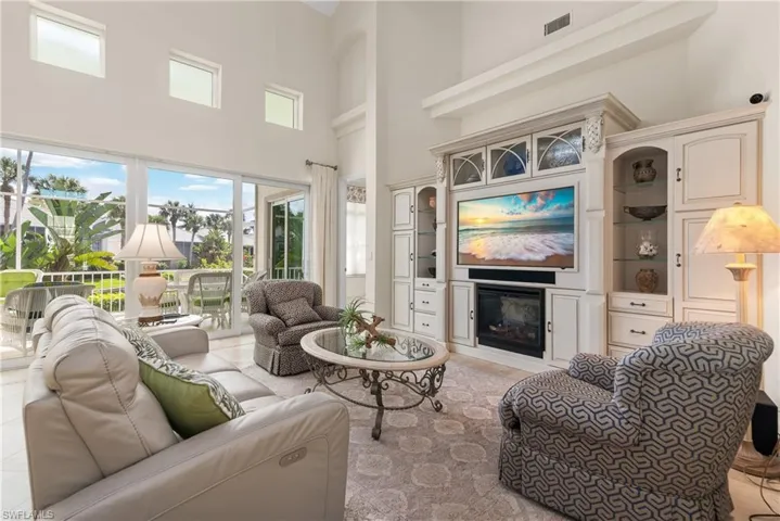 Living room with a towering ceiling, a glass covered fireplace, plenty of natural light, and built in shelves