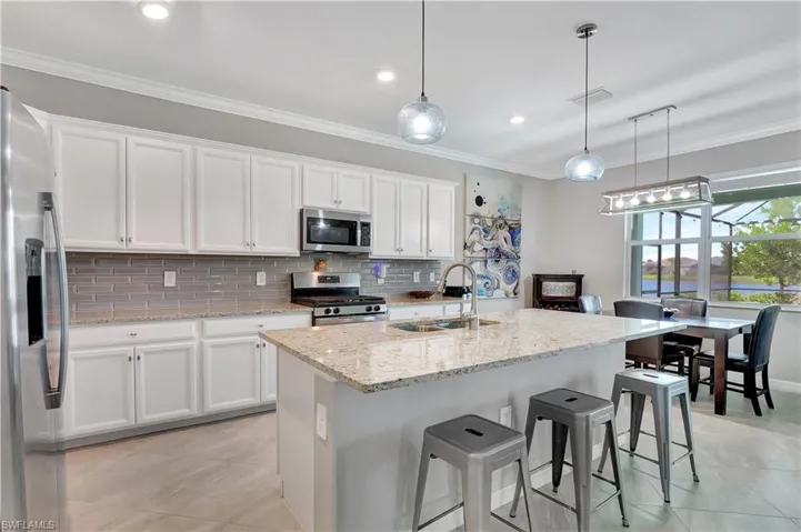 Kitchen with light tile patterned flooring, backsplash, light stone counters, appliances with stainless steel finishes, and sink