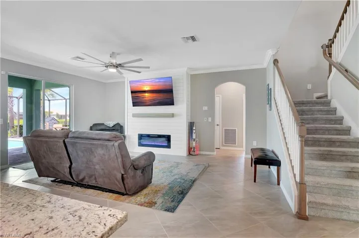 Tiled living room featuring a fireplace, brick wall, ceiling fan, and crown molding