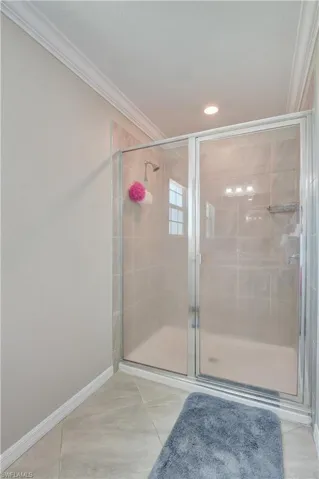 Bathroom featuring a shower with door, tile patterned flooring, and ornamental molding