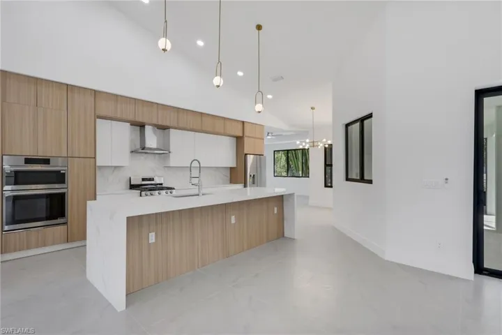 Kitchen featuring lofted ceiling, light stone countertops, a center island with sink, two tone cabinets, and modern cabinets