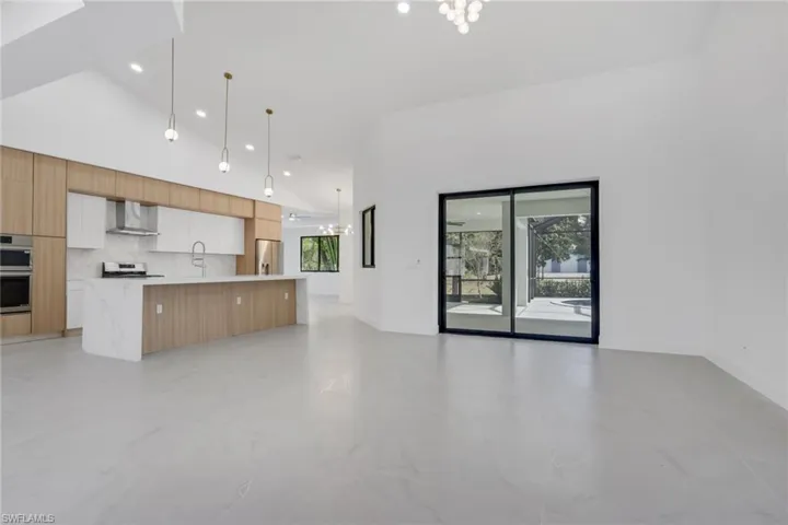 Kitchen featuring modern cabinets, open floor plan, stainless steel appliances, dual tone cabinetry, and light stone counters
