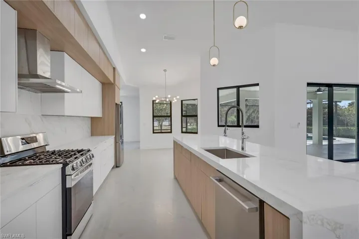 Kitchen featuring two tone color scheme, stainless steel appliances, modern cabinets, light stone counters, and hanging lights