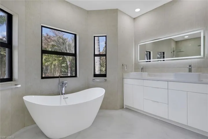 Full bath with double vanity, a soaking tub, tile walls, and light marble finish flooring