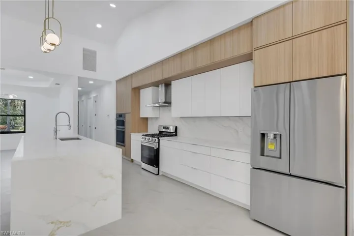 Kitchen featuring two tone cabinetry, stainless steel appliances, pendant lighting, modern cabinets, and light stone countertops
