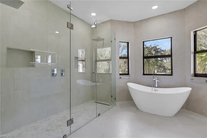 Full bath with double vanity, a soaking tub, tile walls, and light marble finish flooring