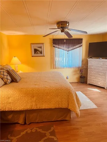 Bedroom with light wood-style floors, ceiling fan, and wooden walls