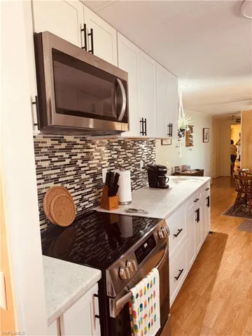 Kitchen with stainless steel appliances, white cabinetry, light wood-style flooring, and a textured ceiling