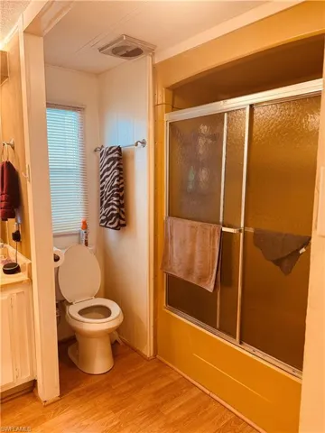 Bathroom with light wood-style floors, combined bath / shower with glass door, and vanity