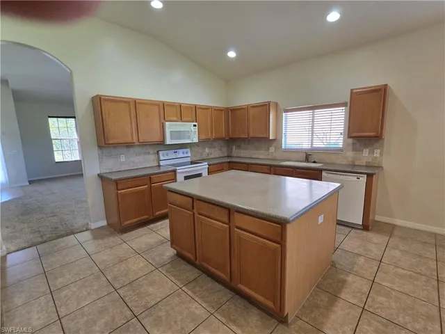Kitchen with arched walkways, tasteful backsplash, a center island, white appliances, and vaulted ceiling