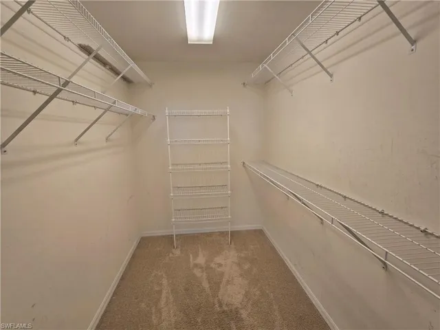 Spacious closet in master bedroom with light colored carpet