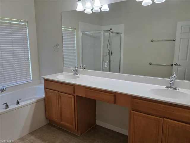 Bathroom featuring a shower stall, dark tile patterned flooring, a bath, double vanity.