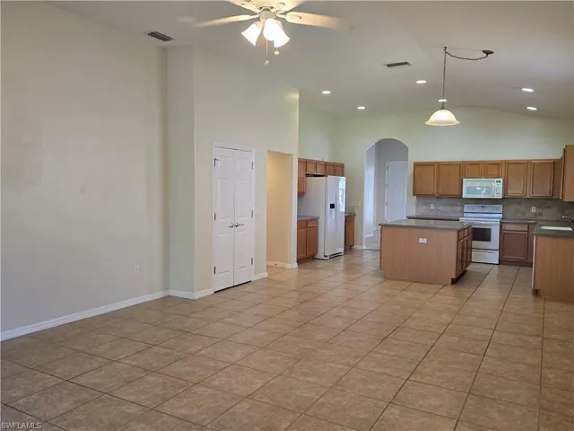 Kitchen featuring arched walkways, backsplash, white appliances, pendant lighting, and high vaulted ceiling