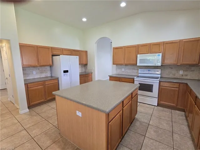 Kitchen featuring white appliances, decorative backsplash, a center island, light tile patterned floors, and high vaulted ceiling
