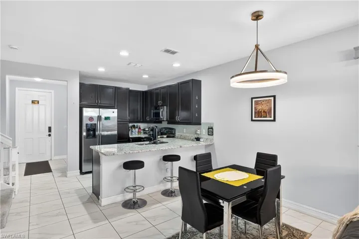 Kitchen featuring dark cabinetry, stainless steel appliances, a peninsula, light stone counters, and a breakfast bar