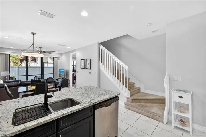 Kitchen featuring light stone countertops, open floor plan, stainless steel dishwasher, ceiling fan, and pendant lighting