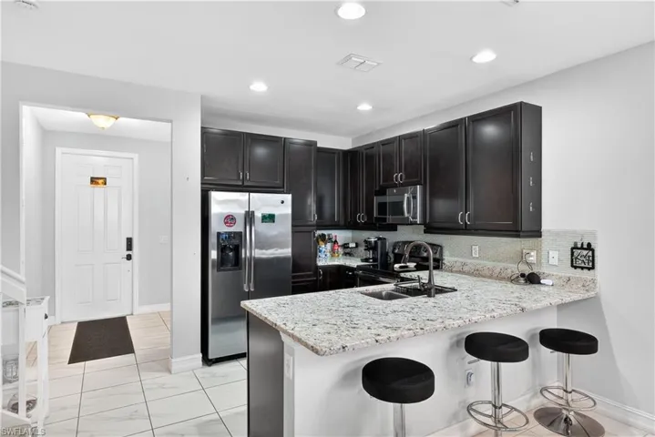 Kitchen featuring stainless steel appliances, a kitchen breakfast bar, a peninsula, light stone counters, and light marble finish floors