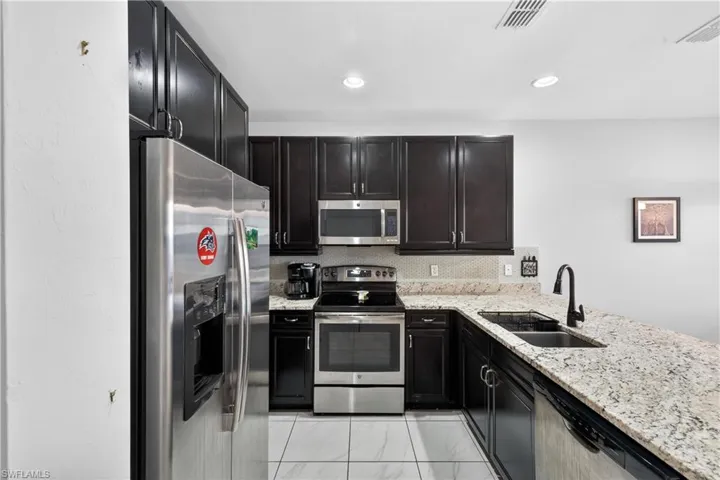 Kitchen with stainless steel appliances, light stone counters, dark cabinets, and recessed lighting