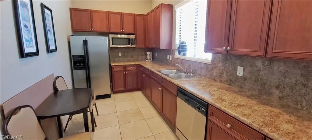 Kitchen with stainless steel appliances, tasteful backsplash, light tile patterned floors, and wood finish cabinetry