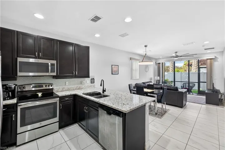 Kitchen with stainless steel appliances, dark cabinets, light stone countertops, a peninsula, and pendant lighting