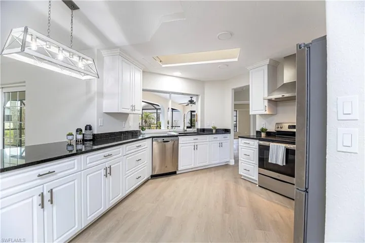 Kitchen with light wood-type flooring, white cabinetry, hanging light fixtures, stainless steel appliances, and ceiling fan