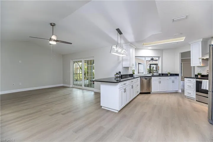 Kitchen with lofted ceiling, kitchen peninsula, white cabinetry, appliances with stainless steel finishes, and light wood-type flooring