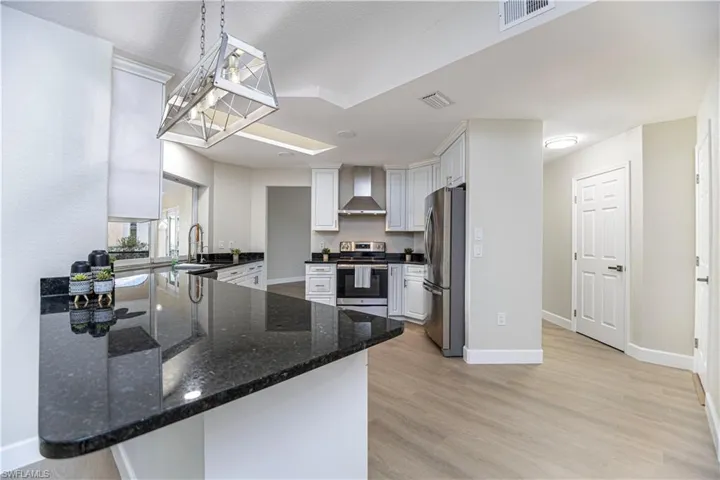 Kitchen with appliances with stainless steel finishes, wall chimney exhaust hood, kitchen peninsula, and white cabinets
