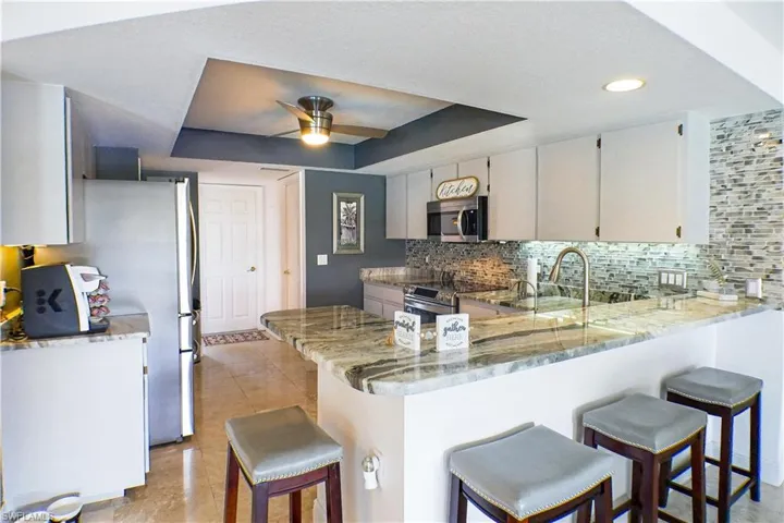 Kitchen with kitchen peninsula, ceiling fan, tasteful backsplash, a raised ceiling, and appliances with stainless steel finishes