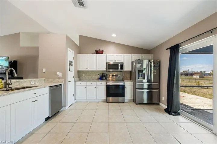 Kitchen featuring visible vents, a sink, appliances with stainless steel finishes, vaulted ceiling, and decorative backsplash