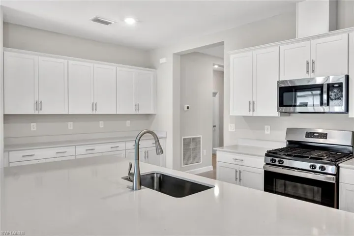 Kitchen featuring stainless steel appliances, white cabinets, and light stone countertops