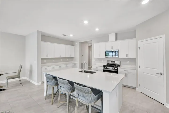 Kitchen featuring stainless steel appliances, a kitchen breakfast bar, white cabinetry, an island with sink, and light stone countertops