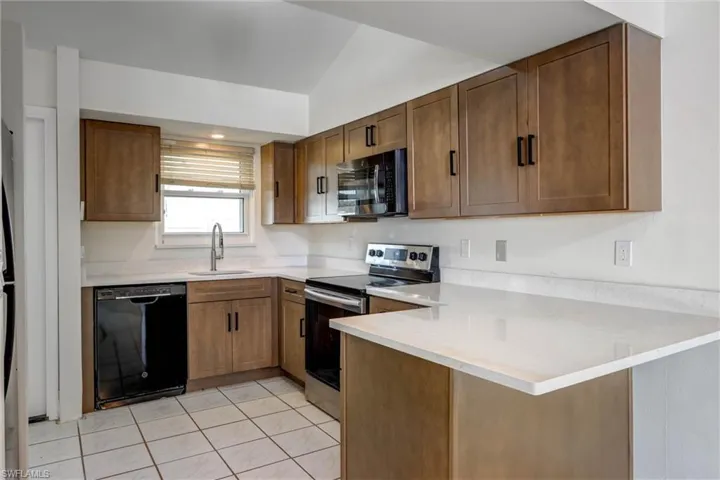 Kitchen featuring wood-finish cabinetry, light-toned countertops, and a full suite of black and stainless steel appliances